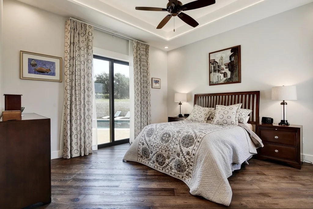 Bedroom with a large bed, nightstands, lamps, a ceiling fan, and sliding glass doors leading outside to a pool.