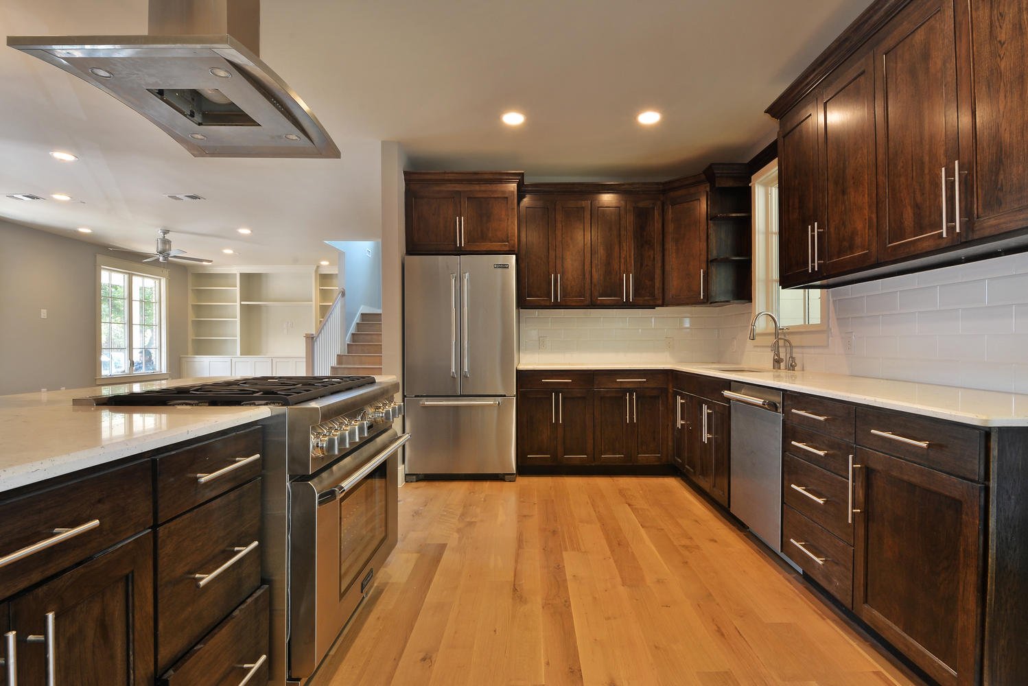 Modern kitchen with dark wooden cabinets, white countertops, stainless steel appliances, hardwood floors, and a window above the sink.