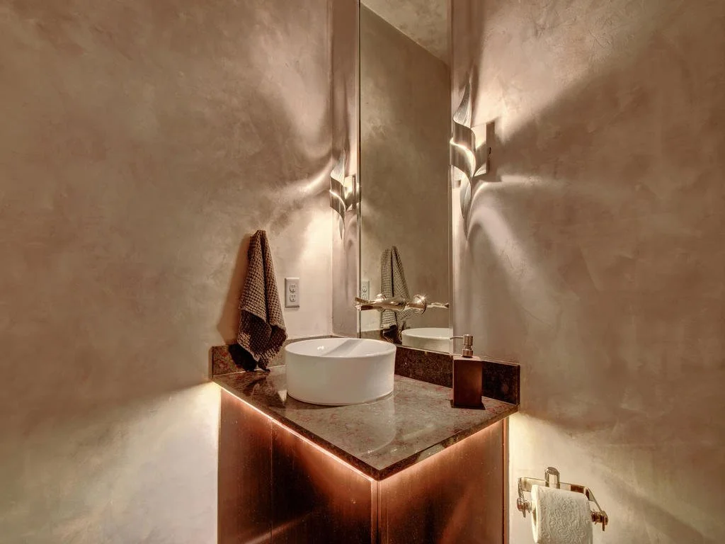 Modern bathroom with a round vessel sink on a dark countertop, beige textured walls, a tall mirror, a wall-mounted faucet, and a towel hanging on the wall.