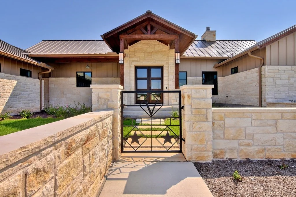 Front view of a modern house with a stone and wood exterior, metal roof, and a small black metal gate with star designs, leading to the entrance