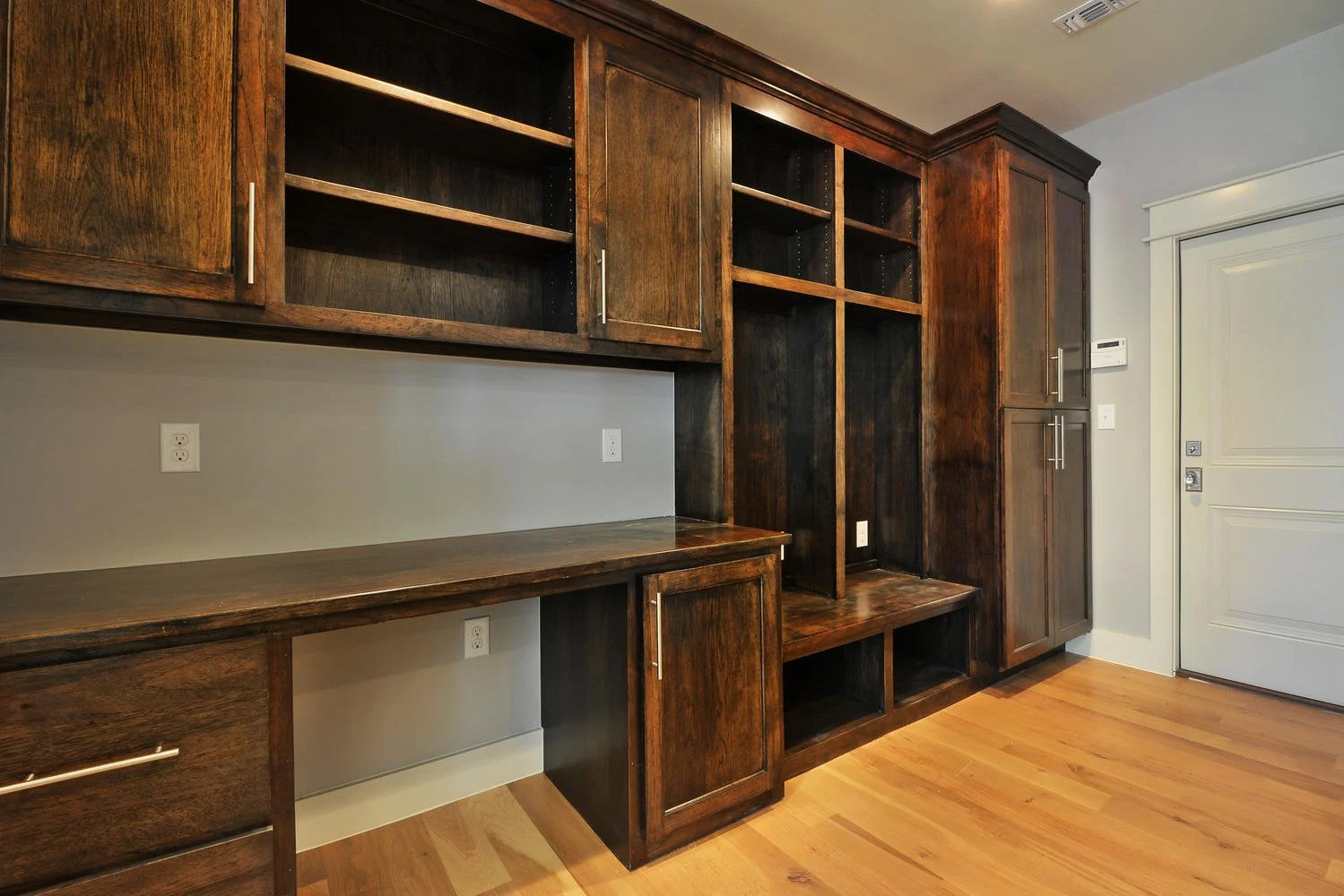 Built-in wooden cabinetry with open shelves, closed cabinets, and a countertop area in a room with wooden flooring and a white door.
