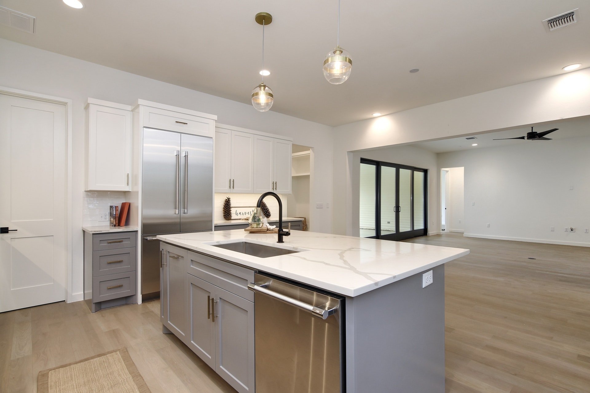 Modern kitchen with white cabinets, stainless steel refrigerator, and a central island with a white marble countertop. Open living space with sliding glass doors leading outside, and light wood flooring.