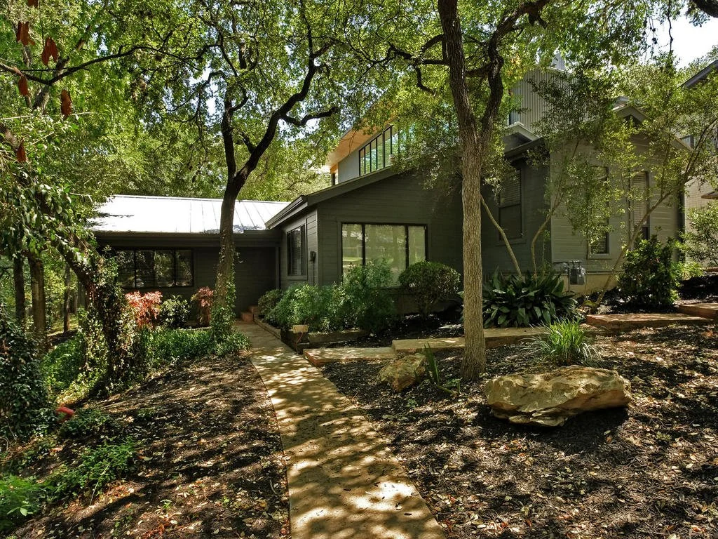 A house surrounded by trees and greenery, with a curved pathway leading to the front door.