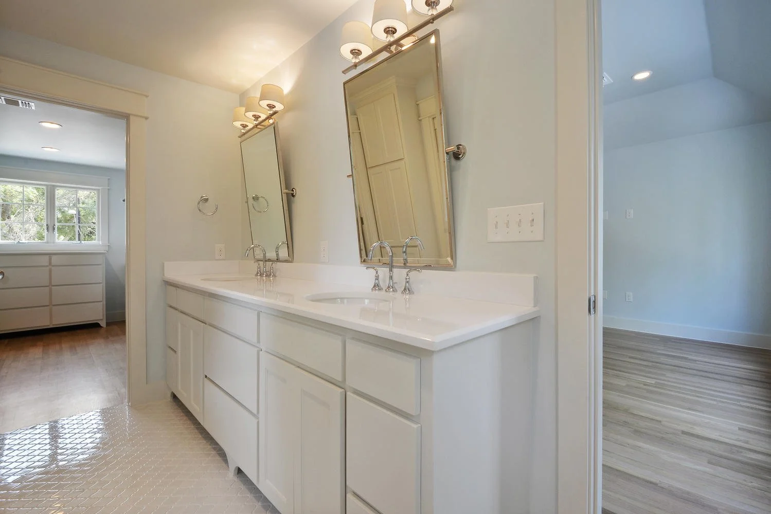 Bathroom with double sinks, white cabinets, framed mirrors, and wall-mounted lights