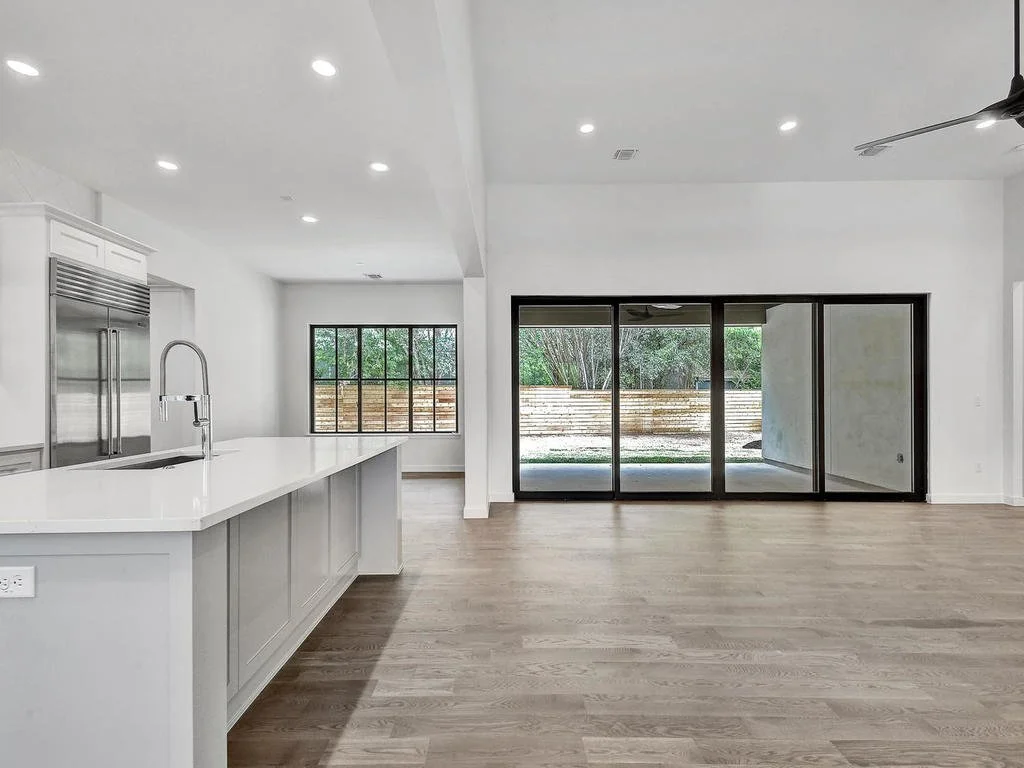 Open-concept kitchen with white countertops, stainless steel appliances, and large sliding glass doors leading to a backyard.