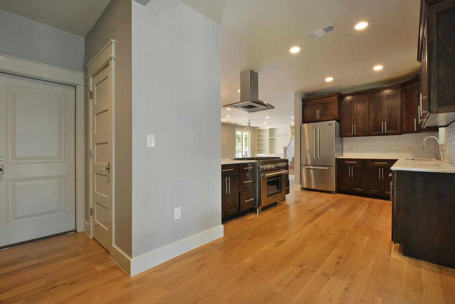 Modern kitchen with dark wooden cabinets, stainless steel appliances, light wood flooring, and a white subway tile backsplash.