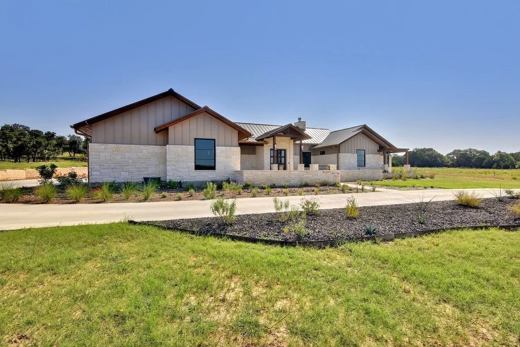 A modern ranch-style house with stone and siding exterior, landscaped front yard, gravel garden beds, and a concrete driveway under a clear blue sky.