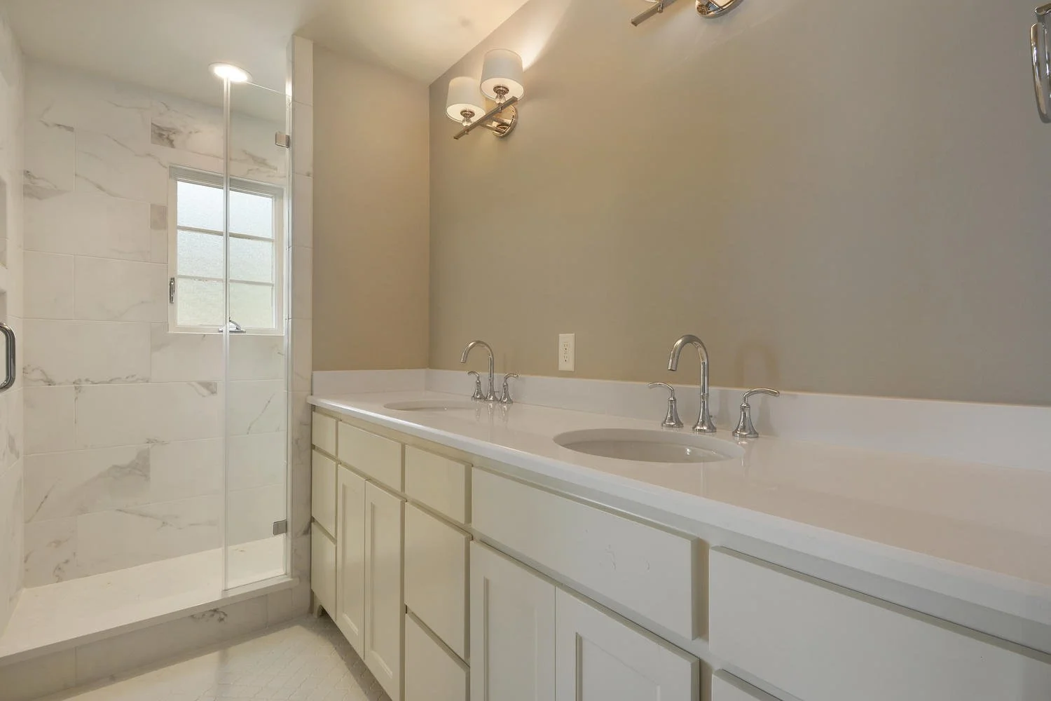 Bathroom with dual sinks, white cabinets, beige walls, and a glass-enclosed shower with marble tiles and a small window.