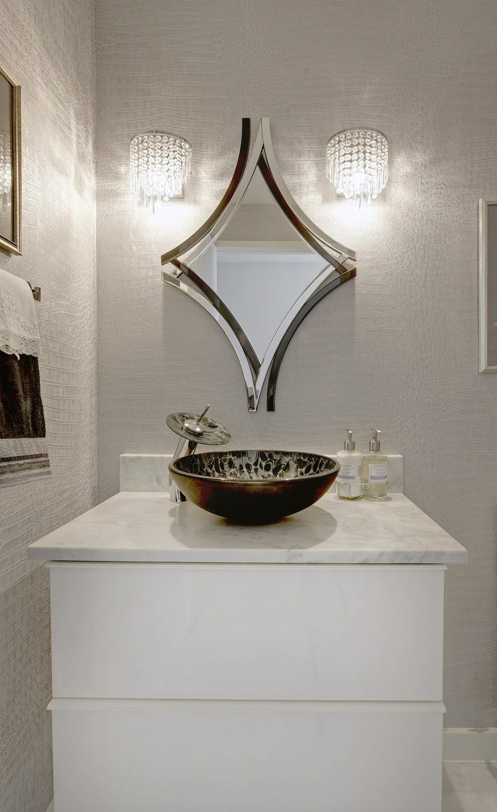 Empty modern bathroom vanity with a black bowl sink, a silver faucet, and two soap dispensers, with a decorative mirror and wall-mounted lights above.