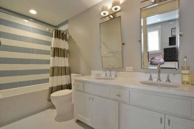 Bathroom with double vanity, two mirrors, two sinks, a toilet, and a shower with striped curtains.