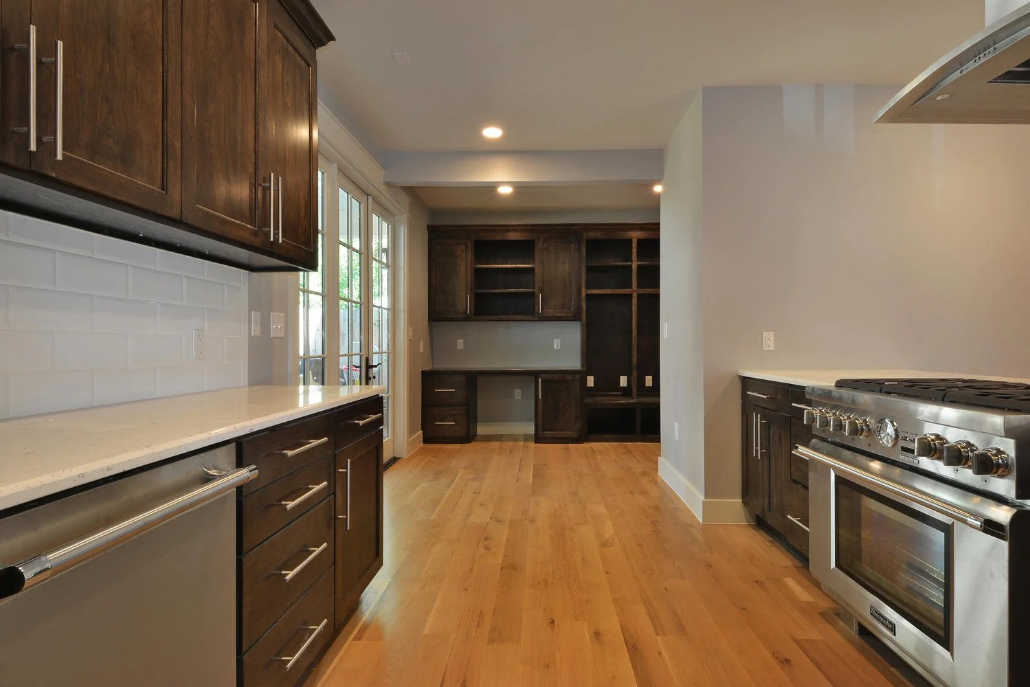 Kitchen with wooden cabinets, stainless steel appliances, white countertops, hardwood floors, and a large window/door leading outside.