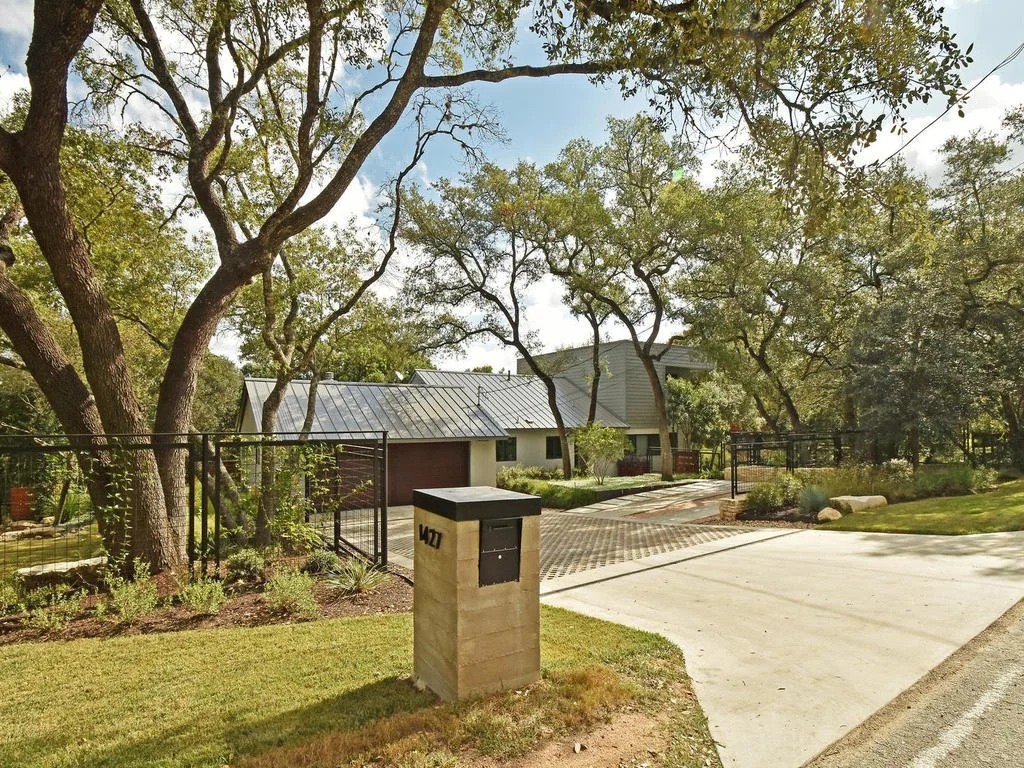 A residential house with a metal roof, surrounded by trees and a lush yard. The house has a driveway and a mailbox marked 427.