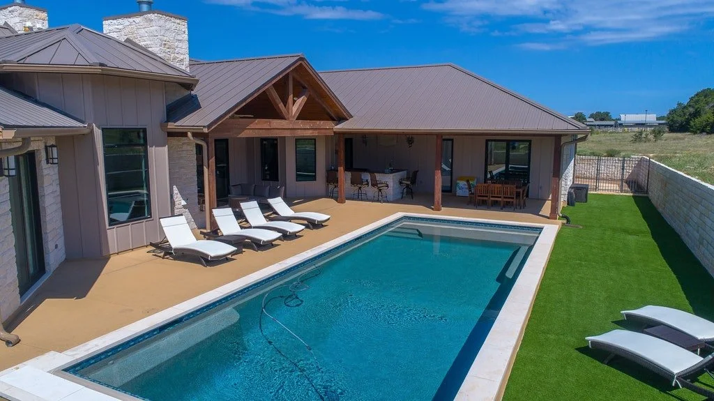 Backyard with swimming pool, lounge chairs, and a covered patio area with furniture surrounded by a brick wall and open field