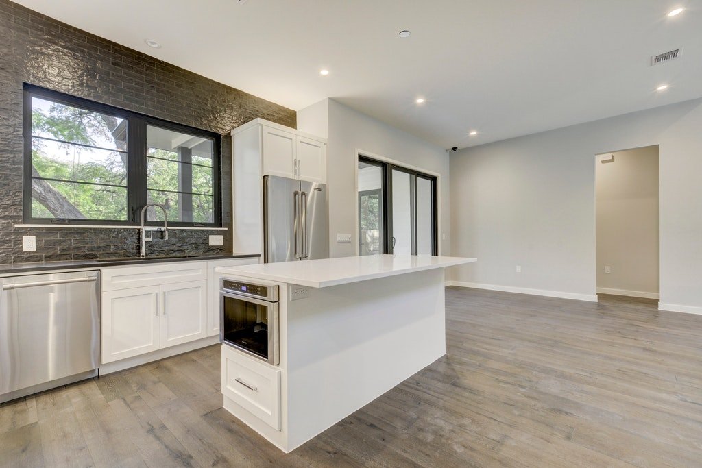 Modern kitchen with black brick wall, white cabinets, stainless steel appliances, and a large island with a built-in microwave.