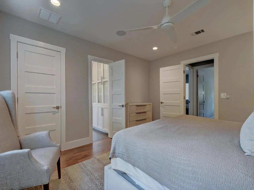 Bedroom with a bed, armchair, ceiling fan, hardwood floors, and open doors leading to closet and bathroom.