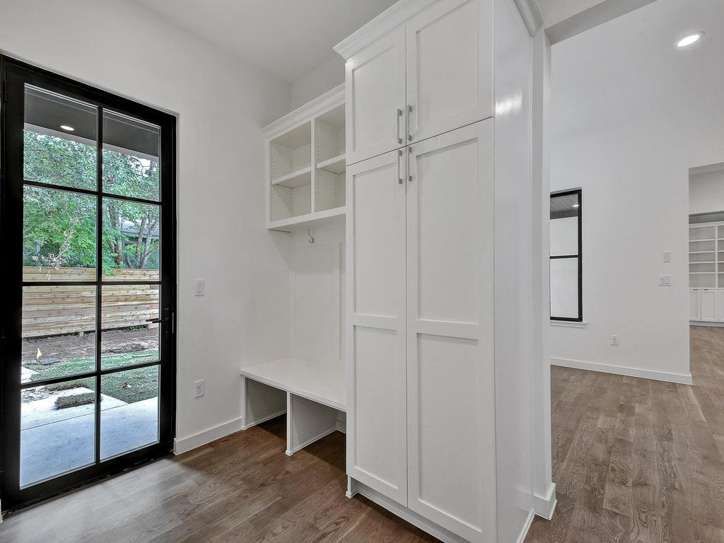 Interior view of a room with white built-in cabinets and open shelves, a black-framed glass door leading outside, and wood flooring.