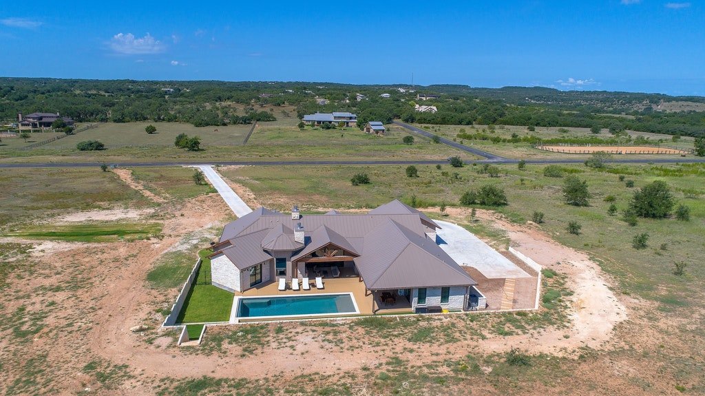 A large house with a pool in a rural area with open land and sparse trees.