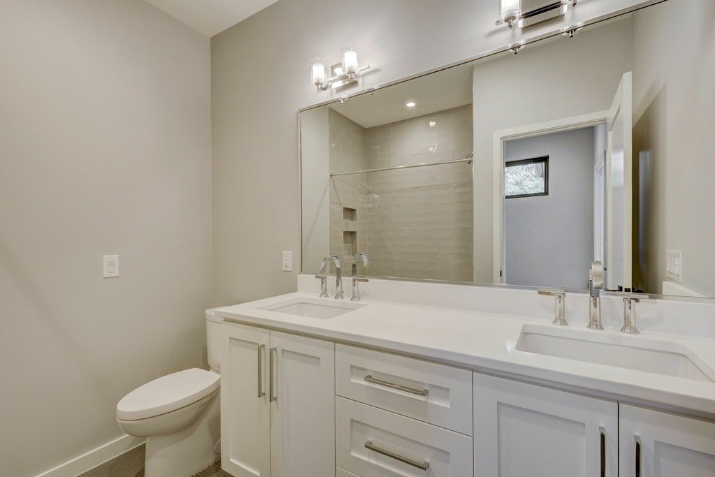 Modern bathroom with dual sinks, large mirror, vanity storage, toilet, and walk-in shower with glass door.