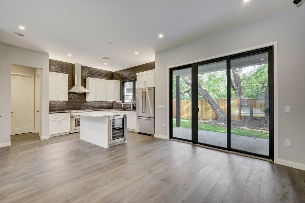 Modern kitchen with white cabinets, a kitchen island, stainless steel appliances, and large sliding glass doors leading to a backyard with trees.