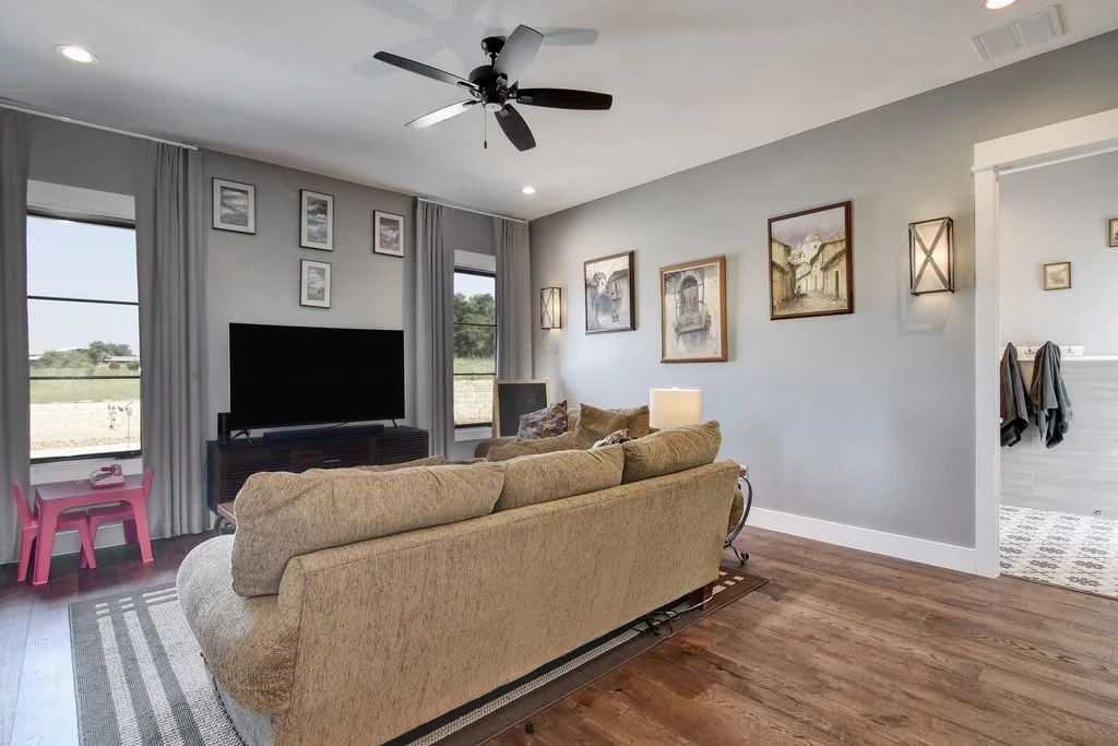 Living room with beige sofa, wall art, TV, and windows with curtains.