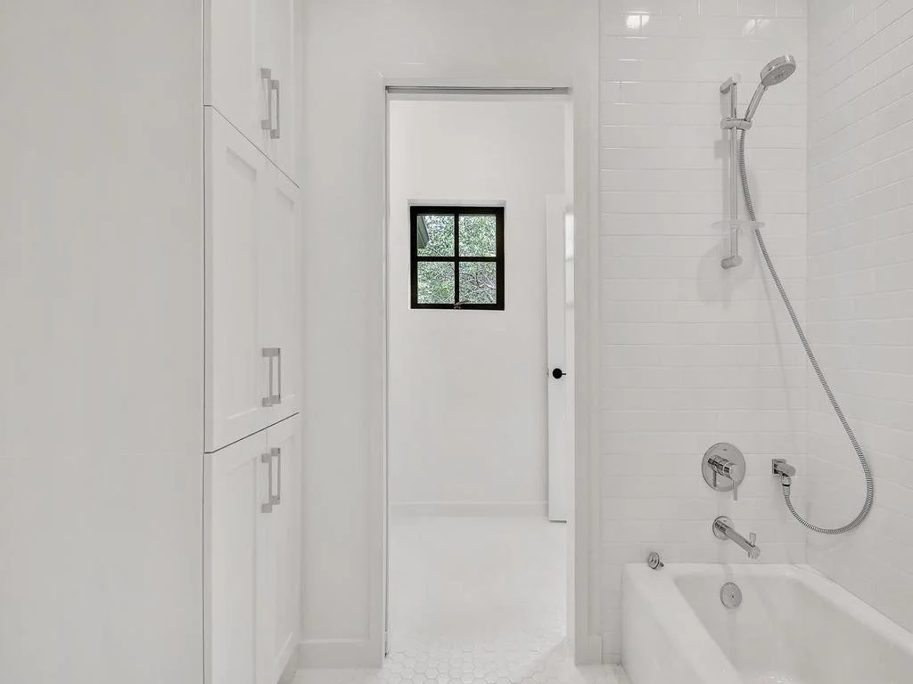 A white bathroom with a bathtub, showerhead, and a small window in the back.