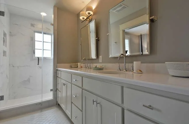 Bathroom with a double vanity, two mirrors, and a shower with a glass door and a window.