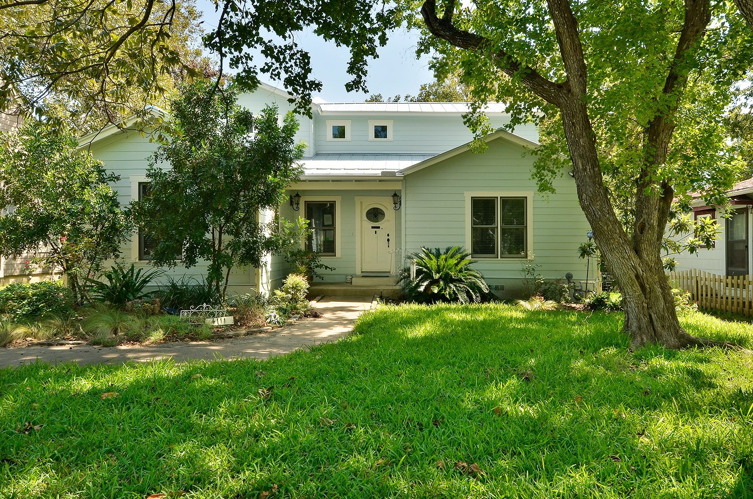 A white house with a front door, multiple windows, and green lawn and trees in the yard.
