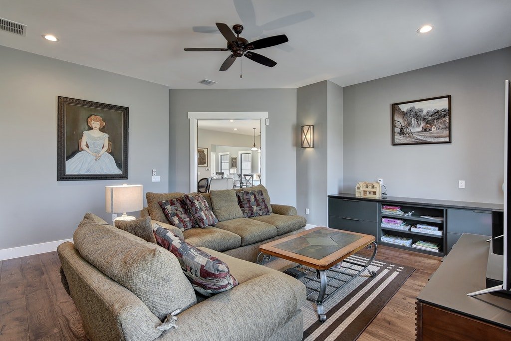 Living room with beige sofas, a wooden coffee table, a flat-screen TV, and wall art, with a doorway leading to a dining area.