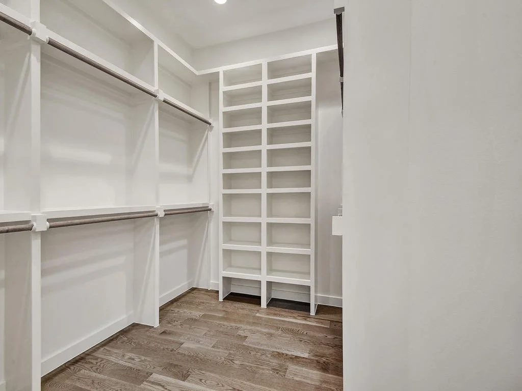 Empty walk-in closet with white shelving and wood floors.
