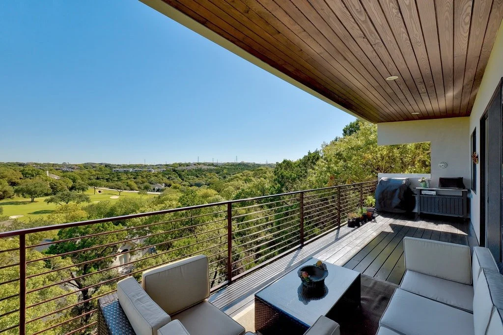 Balcony with white outdoor furniture and view of green trees and distant landscape under a clear blue sky