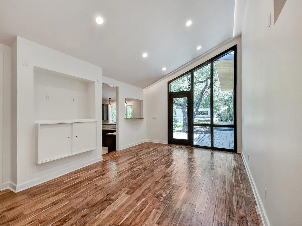 Empty living room with hardwood floors, large glass door, and windows leading to an outdoor deck.