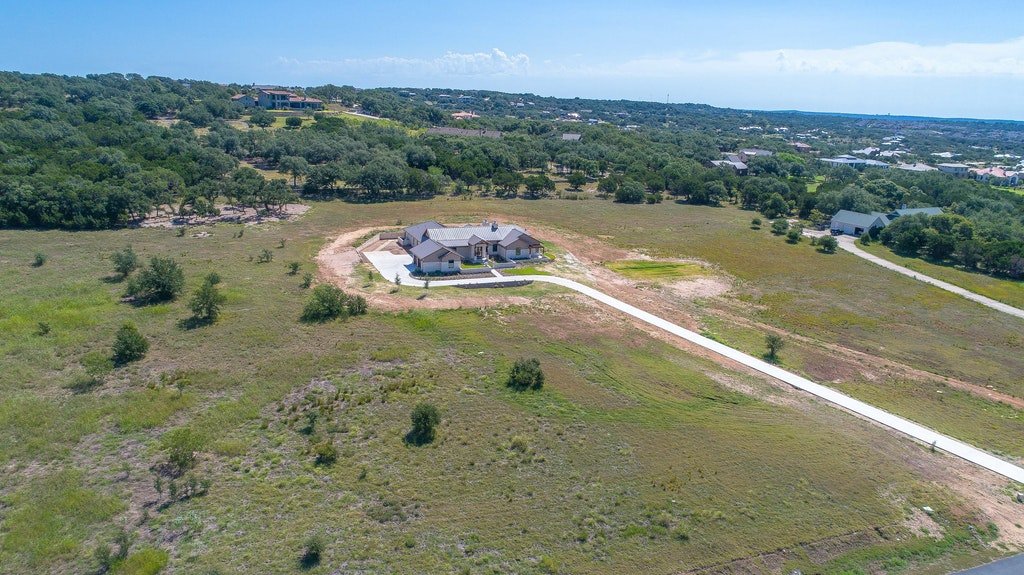 Aerial view of a large house on a spacious, partially developed plot of land with walking paths, surrounded by greenery and other houses in the distance.