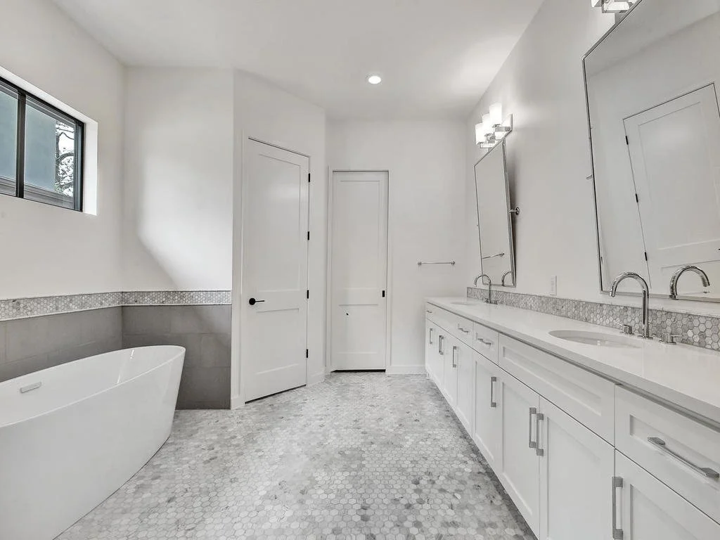 Modern bathroom with a white freestanding bathtub, double vanity with two sinks, two mirrors, and contemporary lighting fixtures.