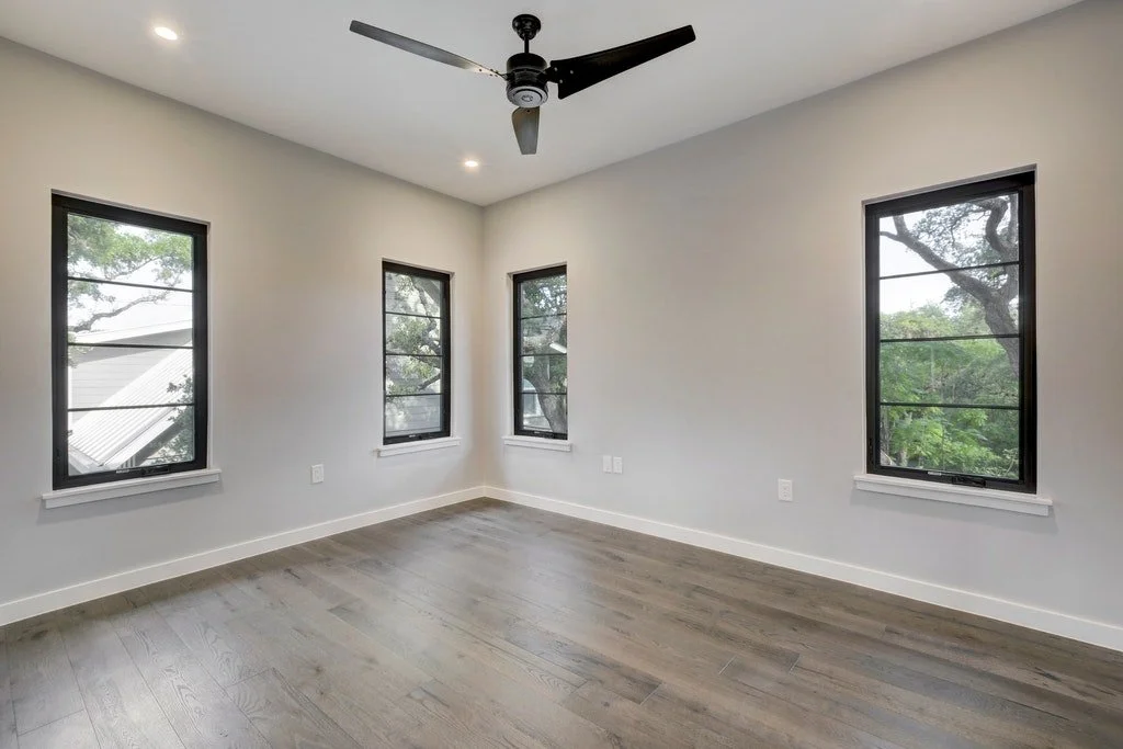 Empty room with three large windows, a ceiling fan, and hardwood floors.