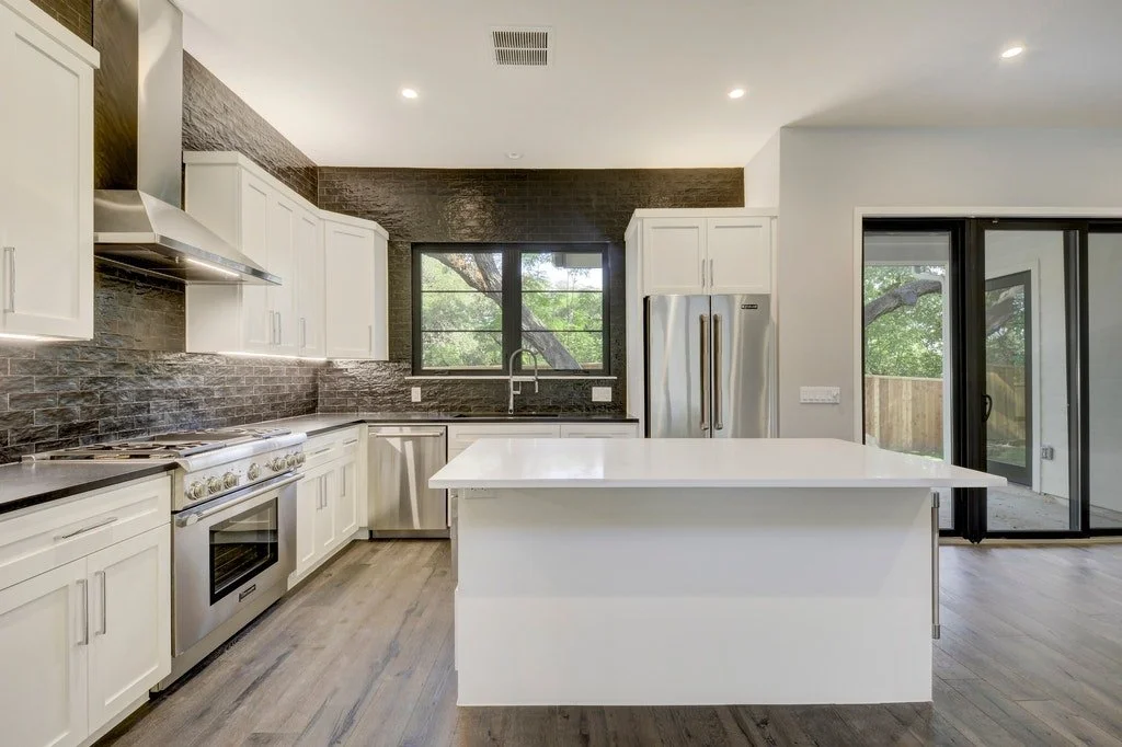 Modern kitchen with white cabinets, black countertops, stainless steel appliances, a large island, and a sliding glass door leading outside.