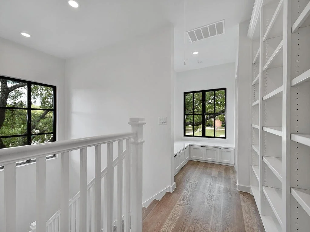 Bright, modern hallway with white walls, black-framed windows, built-in white cabinets, and wooden flooring.