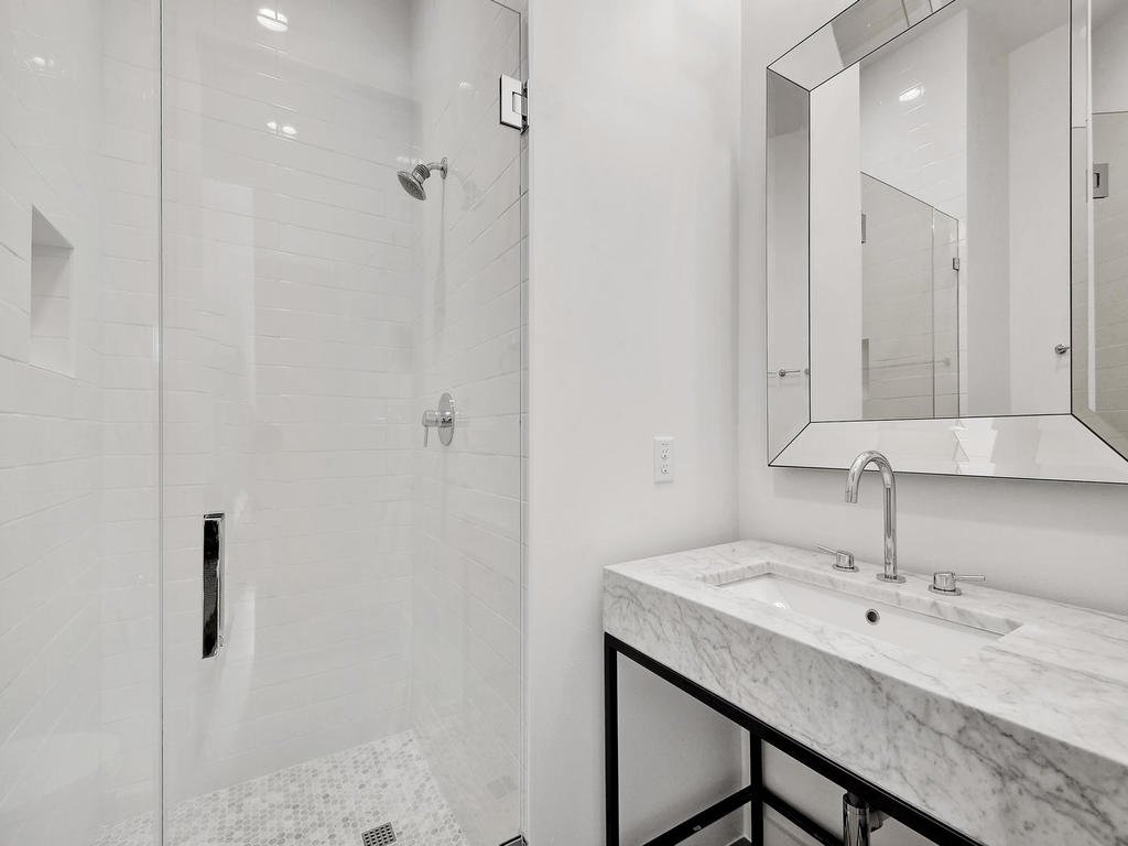 Modern bathroom with a walk-in shower featuring white tiles, and a marble vanity with a large mirror.