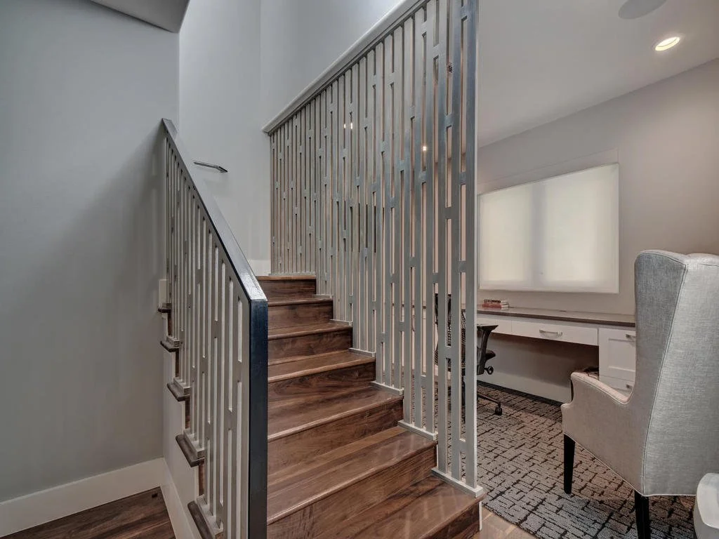 Interior of a modern home with wooden stairs, a white railing, a white built-in desk, and a beige armchair.
