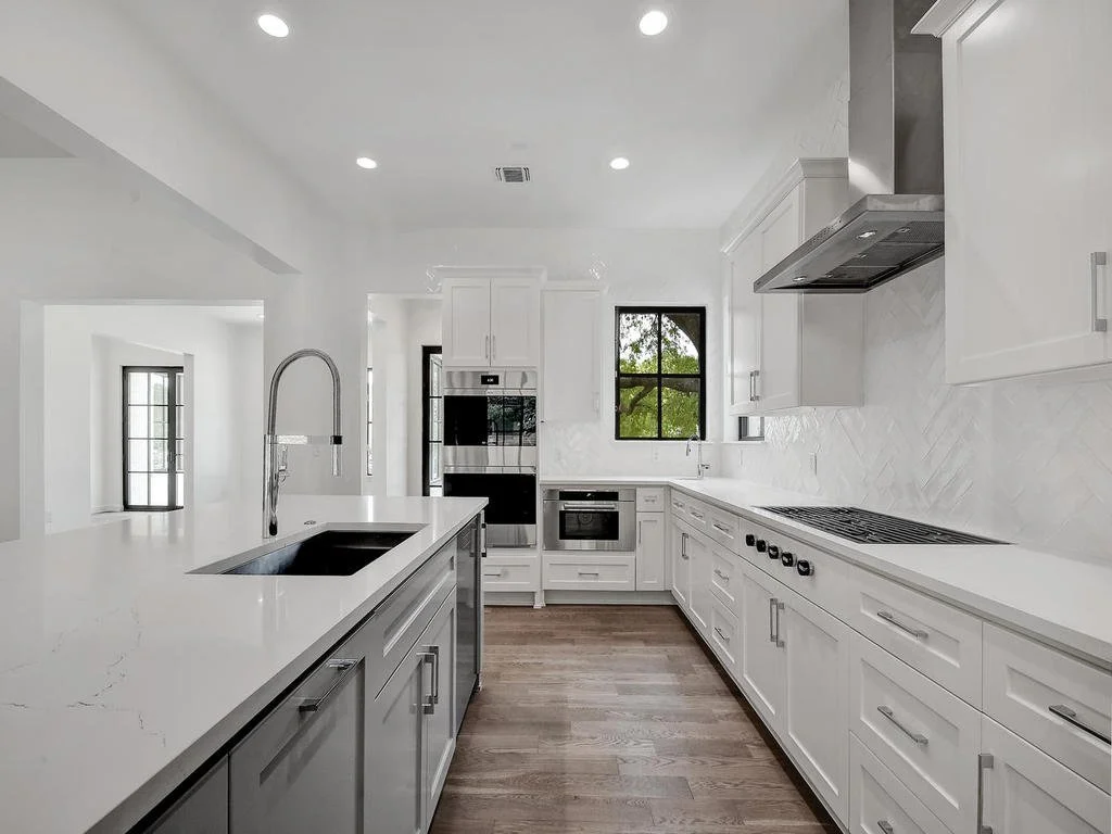 Modern white kitchen with island, stainless steel appliances, and wooden floor.