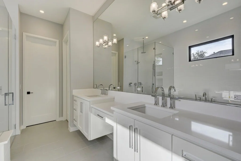 Modern bathroom with double sinks, large mirror, glass shower enclosure, and small window.