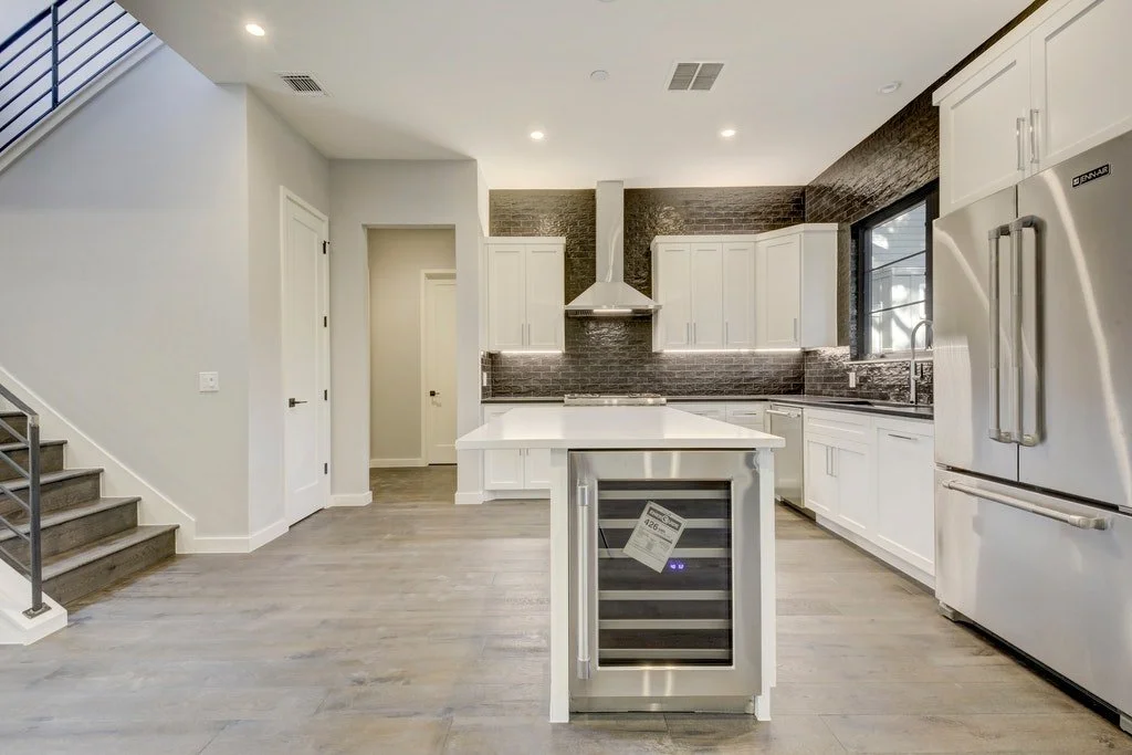 Modern kitchen with white cabinets, stainless steel appliances, a kitchen island, dark brick backsplash, and a window above the sink.
