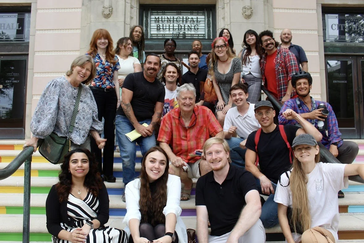 Group of people standing and sitting on colorful stairs in front of a building labeled "Municipal Building." They are smiling and posing for a group photo.