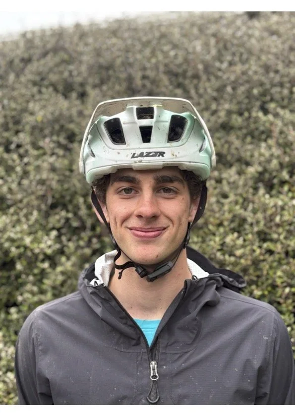 Young man wearing a bike helmet and a dark waterproof jacket outdoors.