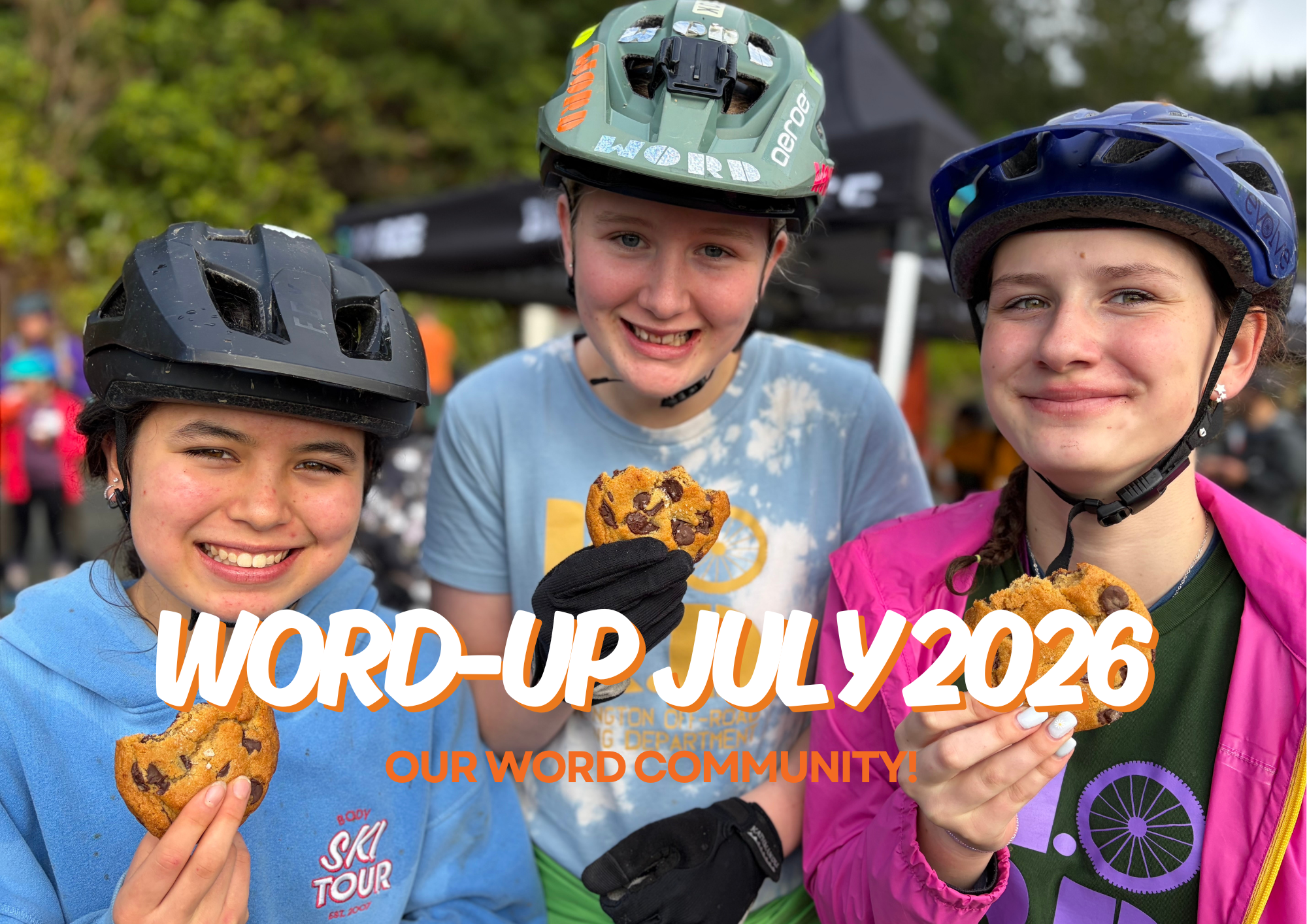 Three young girls wearing bike helmets smiling and holding cookies, with a background of trees and event tents. The image is overlaid with text reading 'WOR# UP JULY 2026' and 'OUR WORD COMMUNITY!'.