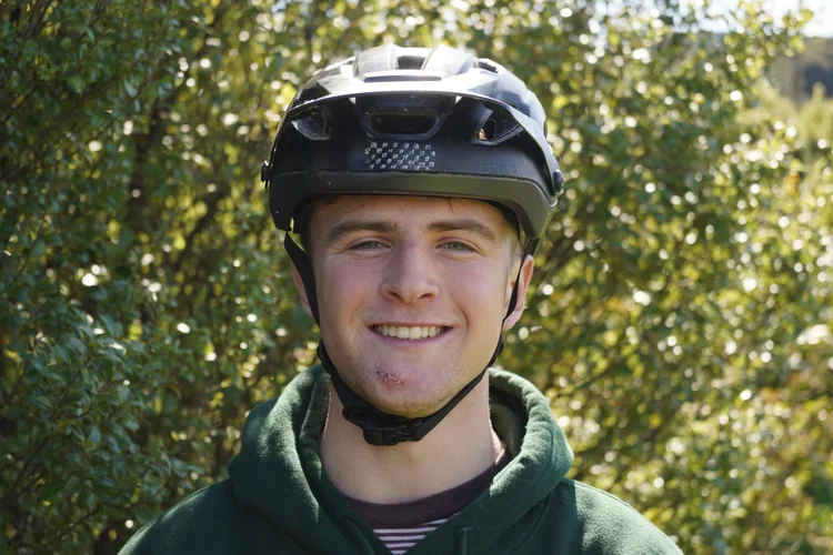 Young man outdoors wearing a bicycle helmet and green hoodie, smiling