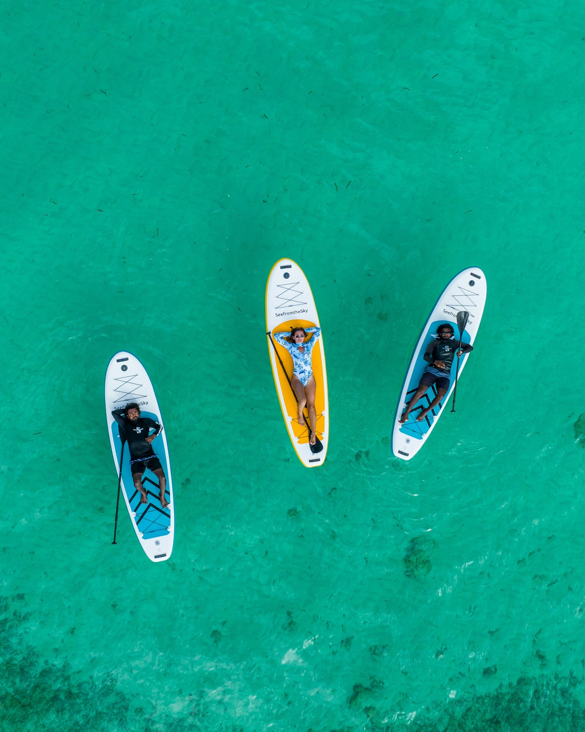 View of three people relaxing on stand-up paddleboards on clear turquoise water