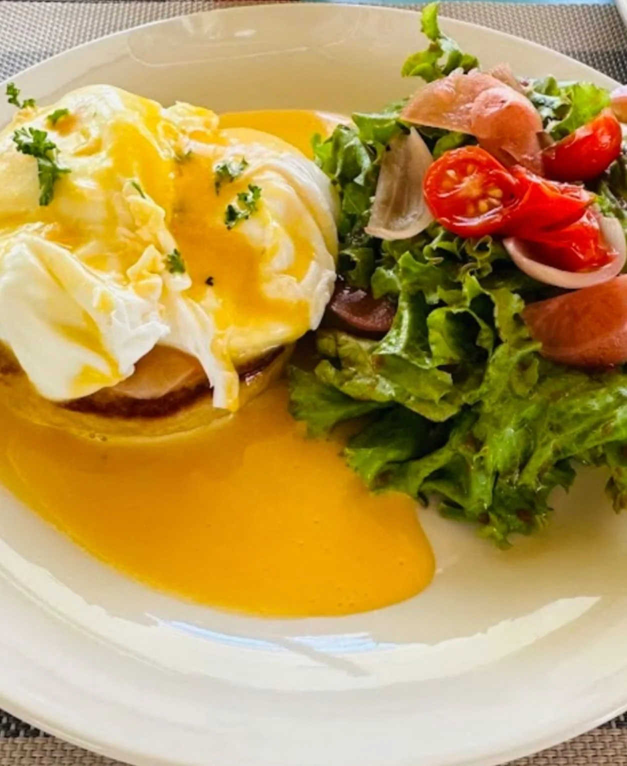 Eggs Benedict with hollandaise sauce and a side salad with cherry tomatoes, lettuce, and onions on a white plate.