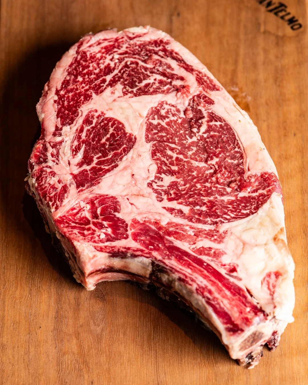 Raw beef steak with marbling on a wooden cutting board.