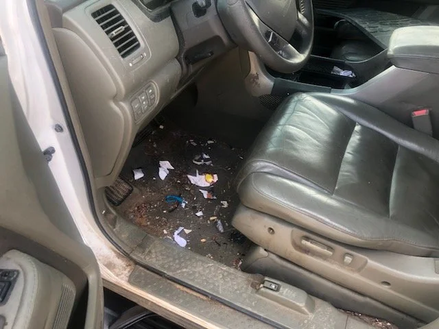 Interior of a vehicle with a dirty floor, paper debris, and a gray leather seat.