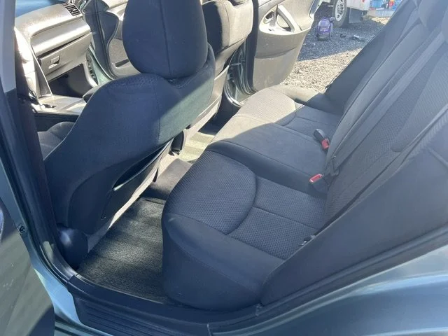 The backseat of a car showing a gray fabric interior with three seats, seat belts, and headrests.
